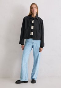 Czarna krótka kurtka z kołnierzem, z dwoma przednimi kieszeniami, noszona na czarno-białym paskowanym swetrze, zestawiona z jasnoniebieskimi dżinsami o szerokich nogawkach i czarnymi butami.