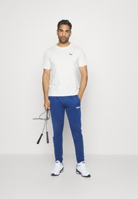 Vit kortärmad T-shirt med svart logotyp, blå träningbyxor med vita sidopaneler, svart hopprep och vita sneakers med blå detaljer.