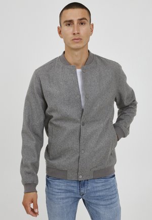 Gray bomber jacket with a textured finish, fitted cuffs, and collar. Features a front snap button closure and side pockets, worn over a white shirt.