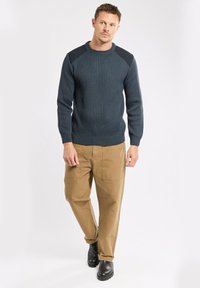Dunkelblauer gerippter Pullover mit kontrastierenden schwarzen Schulterakzenten, kombiniert mit beige Cargo-Hosen und schwarzen Stiefeletten. Schlichtes und funktionales Design.