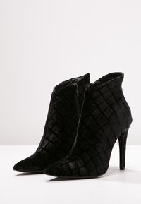 Botas de tobillo negras con punta afilada, superficie texturizada que asemeja piel de cocodrilo, y un elegante tacón de aguja; cuenta con una cremallera lateral.
