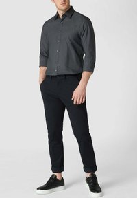 Graues Langarmshirt mit Knopfleiste, schwarze slim-fit Hose und schwarze Sneakers mit weißen Sohlen. Glatte Stoffoberfläche, hochgerollte Ärmeln.