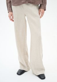 Beige, wijde linnen broek met een gestructureerde afwerking en een subtiele plooi aan de voorkant. Gecombineerd met zwarte, puntige schoenen.