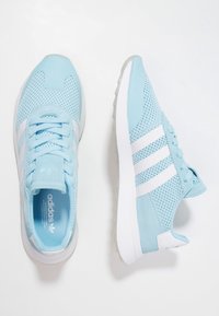 Light blue athletic shoes with mesh fabric, white leather accents, and three white stripes. Cushioned sole and round toe design.