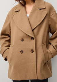 Bruin wollen blend dubbele breasted jas met grote revers, twee voorzakken en bruine knoopdetails. Zachte textuur, ontspannen pasvorm.