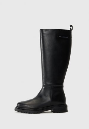 Botas de cuero negras hasta la rodilla con punta redonda, suela resistente y tacón definido. Presentan un lazo en la parte superior y una etiqueta de marca.