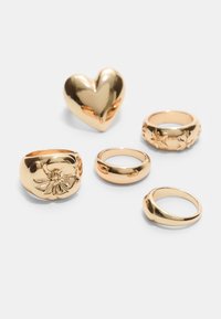 Fem guld ringe: en hjerteformet, en med blomstermotiv, tre glatte bånd i varierende tykkelser, alle med en blank finish.
