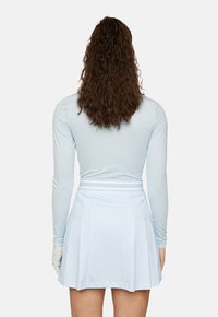 Hellblaues Langarmoberteil mit tailliertem Design, kombiniert mit einem plissierten hellblauen Rock, der eine subtile Musterstruktur und einen kontrastierenden Bund aufweist.