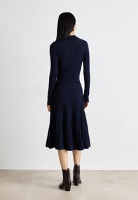 Navy ribbed knit dress with long sleeves, fitted bodice, and a flared pleated skirt. Paired with dark brown ankle boots.