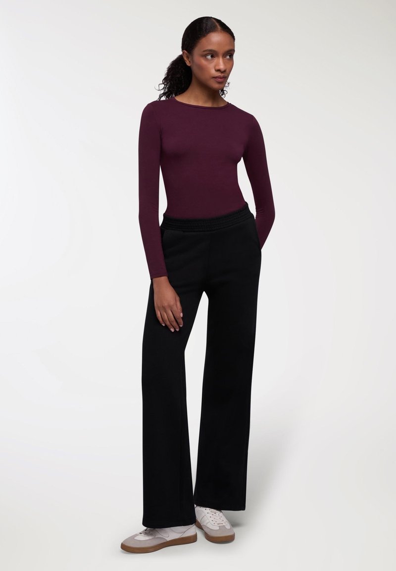 Burgundowy top z długim rękawem połączony z czarnymi, szerokimi spodniami o wysokim stanie i białymi sneakersami, z teksturowanym pasem i gładkim materiałem.