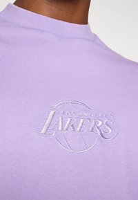 Purple short-sleeve t-shirt made of cotton featuring an embroidered "Los Angeles Lakers" logo with a basketball design.