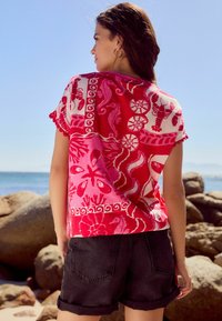 Rød og pink mønstret skjorte med maritime motiver; løs pasform, kortærmet, bølget kant, parret med sorte denimshorts.