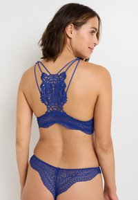 Set di lingerie in pizzo blu con un intricato design di tigre sulla schiena, spalline regolabili e bordi ondulati sulla vita.