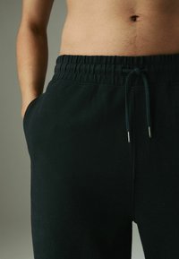 Pantalones jogger negros de textura con cintura elástica, cierre con cordón y bolsillos laterales. La tela parece suave y transpirable.