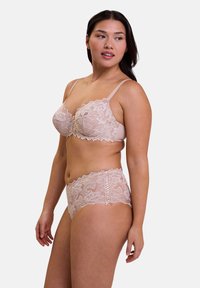 Set di lingerie in pizzo di un delicato beige. Il reggiseno presenta motivi floreali e spalline regolabili. Slip a vita alta con dettagli in pizzo e bordi scallop.