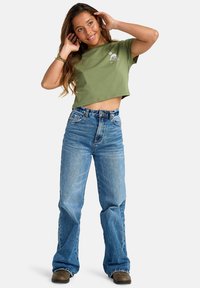 Olive green cropped t-shirt with a front graphic, paired with high-waisted blue denim flared jeans and brown footwear.