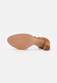 Scarpa con tacco alto in suede color cammello, dotata di suola in gomma texturizzata e tacco sottile. La soletta presenta un dettaglio con il logo distintivo.