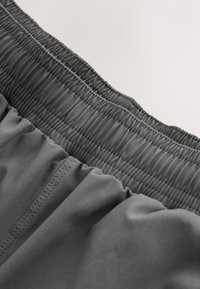 Ceinture élastique gris foncé avec plusieurs rangées de coutures sur un tissu léger, créant un ajustement froncé et flexible.