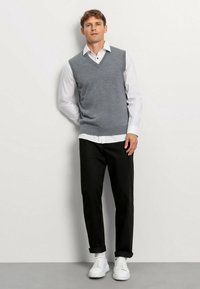 Grijze v-halstrui over een wit overhemdbloesje, gecombineerd met zwarte broek en witte sneakers. Gladde textuur en casual ontwerp.