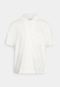 Biała koszulka polo z krótkim rękawem, wykonana z teksturowanej tkaniny. Posiada zapięcie na guziki z przodu, klasyczny kołnierzyk oraz kieszeń na piersi.