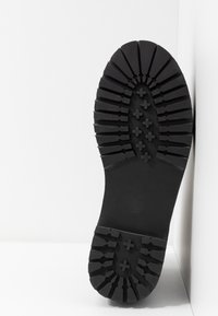 Suela de bota de goma negra con tacos profundos y mejorados y patrones en cruz para un agarre mejorado. El material parece duradero con una superficie texturada.