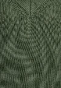 Pull en tricot avec un col en V profond, réalisé en fil vert texturé, présentant un motif côtelé sur toute la surface. Mailles uniformément espacées.