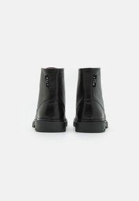 Stivali alla caviglia in pelle nera con finitura testurizzata, suola piatta in gomma e dettagli cuciti. Presenta il brand sul tallone.