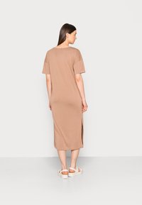 Vestido bege de mangas curtas com um corte descontraído, comprimento até à meia-perna, rachas laterais e textura suave. Combinado com sandálias brancas chunky.