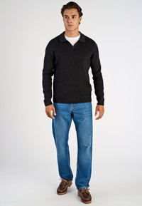 Schwarzer Rippstrickpullover mit V-Ausschnitt und Kragen, kombiniert mit hellblauen Jeans und braunen Schnürschuhen.