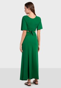 Abito maxi verde con maniche a campana corte, corpetto aderente e dettaglio legato sul retro. Realizzato in tessuto liscio e elasticizzato.
