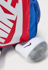 Crvena i plava ruksak s bijelim logotipom, s plišastom nogom sivi potplat i crnim Nike swoosh detaljem. Dizajn s teksturiranom tkaninom.