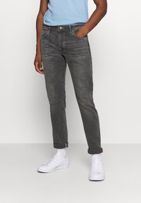 Šedé džíny z denimu s úzkým střihem, pěti kapsami, manžetou na lemu a jemnou vybledlou texturou, doplněné bílými teniskami.