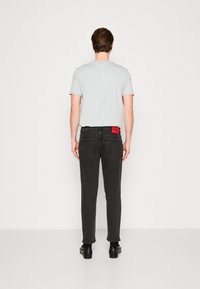 Harmaa t-paita yhdistettynä mustiin farkkuihin. Farkuissa on takana punainen logotarra, suora lahkeensuu ja sileä, yksivärinen pinta.