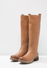 Bottes en cuir marron hautes avec un bout arrondi, une fermeture éclair sur le côté et une semelle texturée. Les coutures à l'avant ajoutent un intérêt visuel.