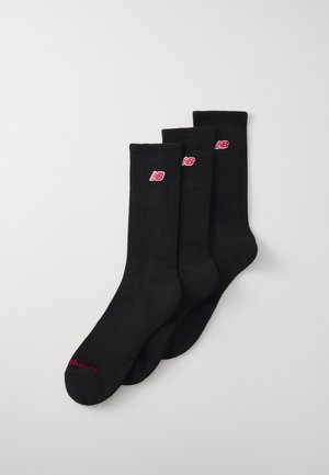 Calcetines de tripulación negros hechos de tela acanalada. Presentan un logo rojo en cada calcetín y texto rojo adicional en la puntera. Conjunto de tres pares.