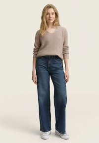 Pull côtelé beige avec un col en V, associé à un jean large taille haute bleu foncé, porté avec des baskets blanches. Texture douce et coupe décontractée.