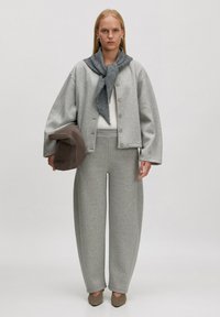 Lichtgrijze, oversized sweatshirt met een ronde kraag en knopen, gecombineerd met bijpassende ruime sweatpants. Een grijze sjaal is om de hals geknoopt.