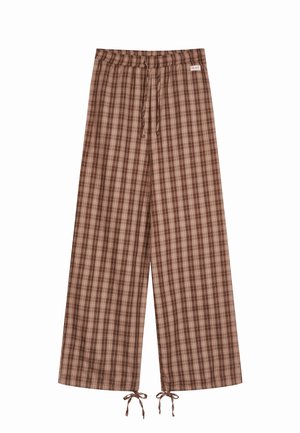 Brązowe szerokie spodnie w kratę z elastycznym pasem, sznurkami do ściągania przy nogawkach oraz małą metką na górnej prawej stronie pasa.