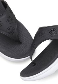 Mustat flip-flopit, joissa on rei'itetty kukkakuvio, teksturoitu kumipohja ja valkoinen välipohja. Silkkiset hihnat ja muotoiltu pohja mukavuutta varten.