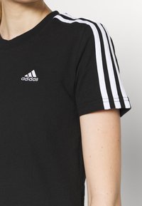 Svart t-shirt i bomull med vit trestripesdesign på ärmarna och en broderad Adidas-logotyp framtill. Korta ärmar och rund hals.
