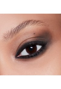 Gros plan sur un œil avec un eye-liner noir et un ombre à paupières ; iris marron foncé, cils bien définis et teint de peau marron clair avec un subtil détail au niveau des sourcils.