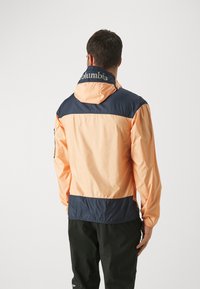 Chaqueta ligera e impermeable con un diseño de bloques de color melocotón y marino, capucha ajustable y puños elásticos. Logo de Columbia en la parte posterior.