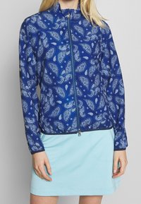 Modrá zipová bunda s paisley vzorem v bílé barvě, vyrobená z lehké tkaniny se stojáčkovým límcem a elastickým lemem.