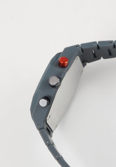 Gray watch with a rectangular metal case, silicone strap, and three buttons: one red, one silver, one black.