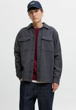 Gray wool shirt jacket with two chest pockets, black buttons, and a collared neck, worn over a maroon sweater and dark jeans.