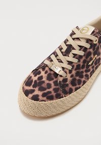 Baskets avec semelle tissée beige et lacets beiges, présentant un tissu à imprimé léopard marron et noir ainsi que des accents de logo dorés sur la languette et le côté.