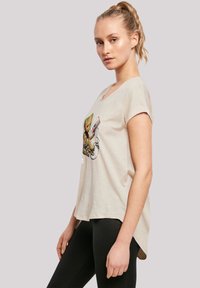 Beige short-sleeve t-shirt with a rounded neckline featuring an illustrated character holding a cassette tape, paired with black leggings.