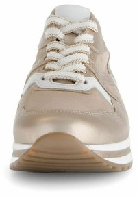 Scarpa sportiva beige con accenti metallici, dotata di lacci bianchi, linguetta imbottita e suola testurizzata con un design a strati.