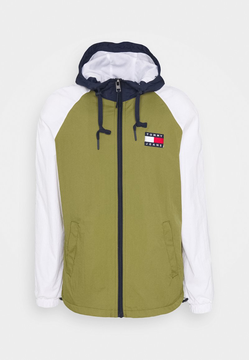 Giacca verde oliva con maniche bianche, cappuccio blu navy, zip frontale e tasche laterali. Presenta il logo "TOMMY JEANS" sul petto. Tessuto liscio.