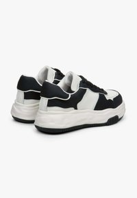 Czarno-biała sneaker z grubą podeszwą, teksturowanymi materiałami, zakrzywionym kształtem i kontrastującymi panelami. Posiada sznurowane zapięcie i wyściełany kołnierz.